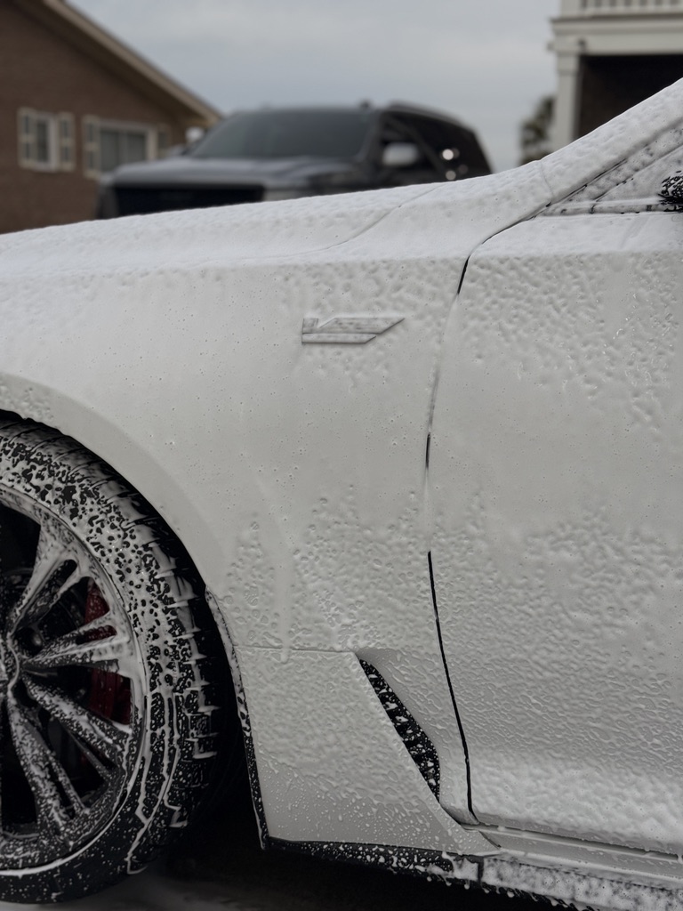 Foam covering a Cadillac front fender and wheel during washing